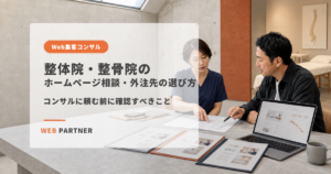 整体院の女性院長が、施術室を背景にWeb担当者とホームページ制作の提案書を比較している様子