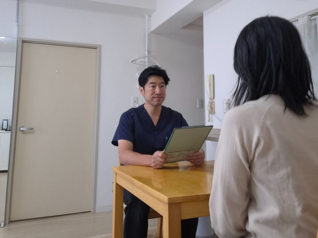朝霞台整体ラボの院長が、施術前にテーブル越しで来院者の話を聞いている様子